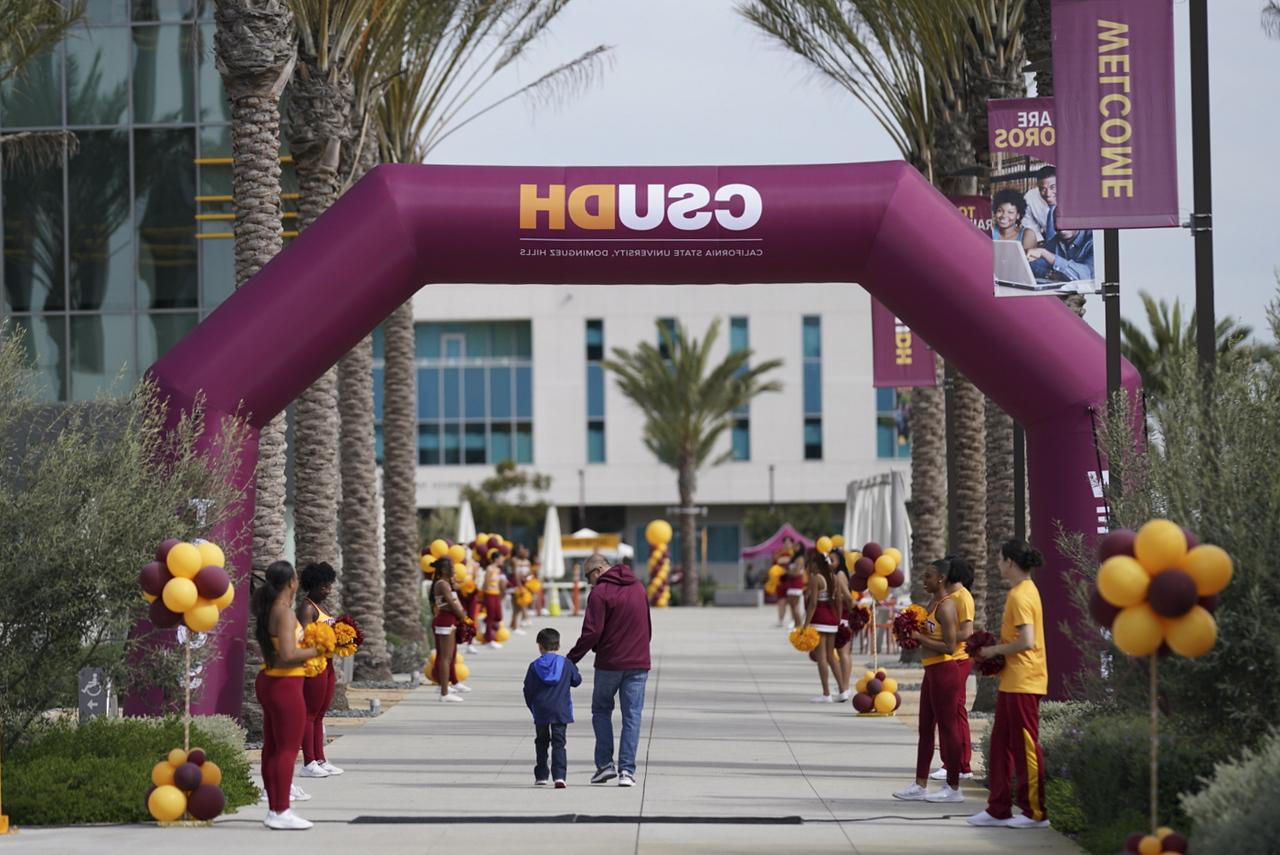 Alum and child walking under CSUDH arch at Homecoming